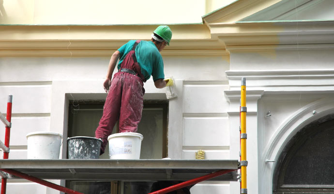 a person is painting the exterior wall of a house standing on scaffolding