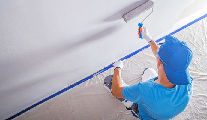 a person painting a interior wall of a room using a roller brush